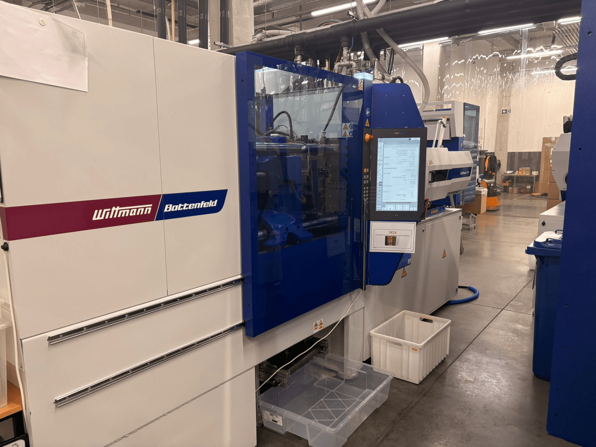 Wittmann Battenfeld spuitgietmachine, vooraanzicht, met een digitaal bedieningspaneel en verschillende veiligheidslabels.
