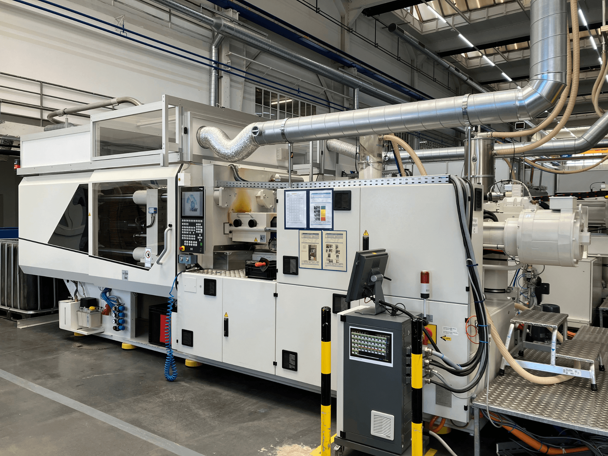 Vooraanzicht van een industriële machine met bedieningspaneel, leidingen en beeldschermen, met een strak wit ontwerp en technische details.