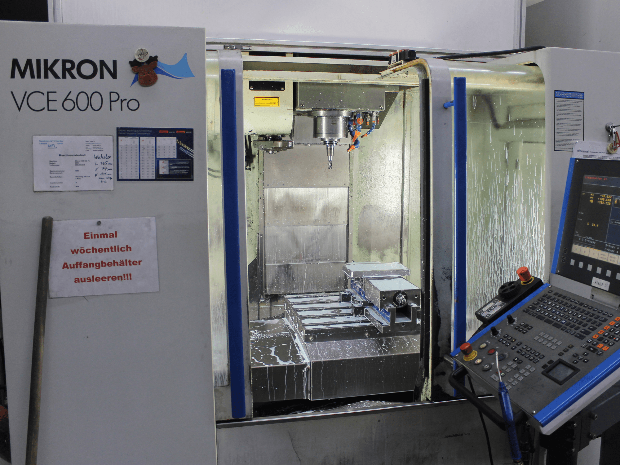 Mikron VCE 600 Pro bewerkingscentrum, vooraanzicht, met snijgereedschappen, koelvloeistofnevel en bedieningspaneel met knoppen.