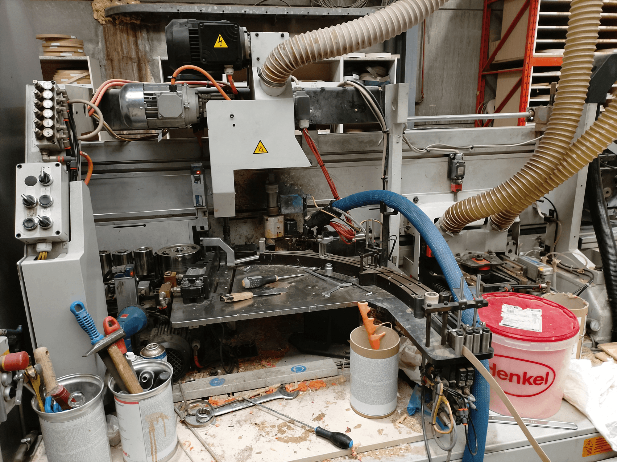 BIESSE Edge Stram B1 kantenaanlijmmachine in vooraanzicht, met machines, slangen en werkgereedschap te midden van houtsnippers.