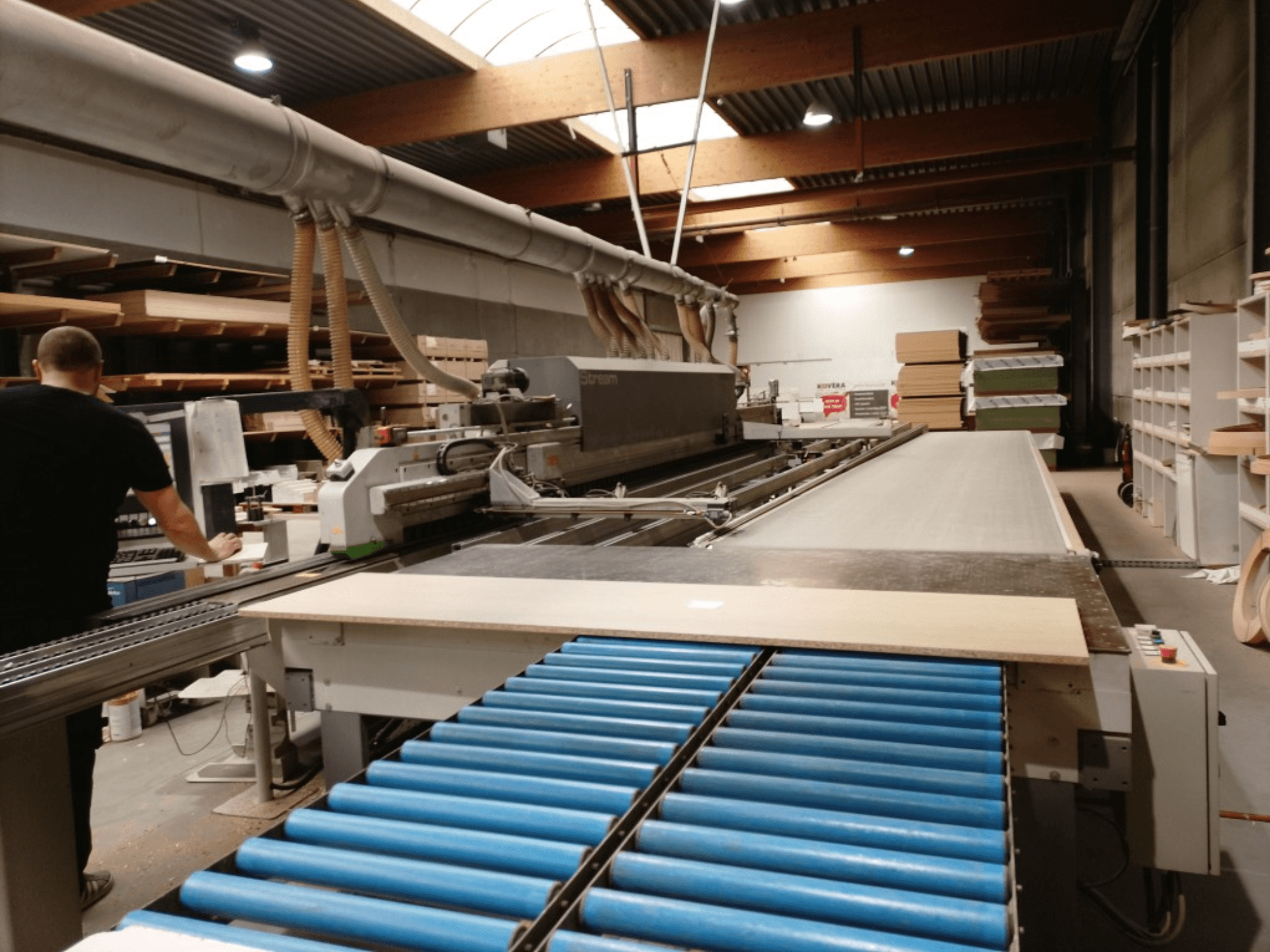 BIESSE Edge Stream B1 kantenaanlijmmachine, zijaanzicht met operator, blauwe rollen en houten paneel op transportband.