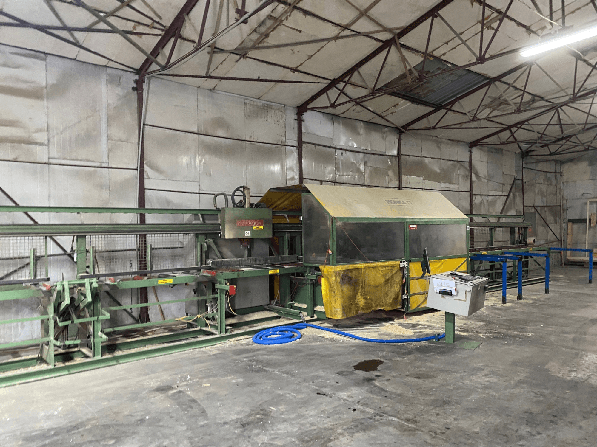 CNC houtbewerkingscentrum HUNDEGGER K1 in een werkplaats, zijaanzicht met machines, bedieningselementen en zaagsel op de vloer.