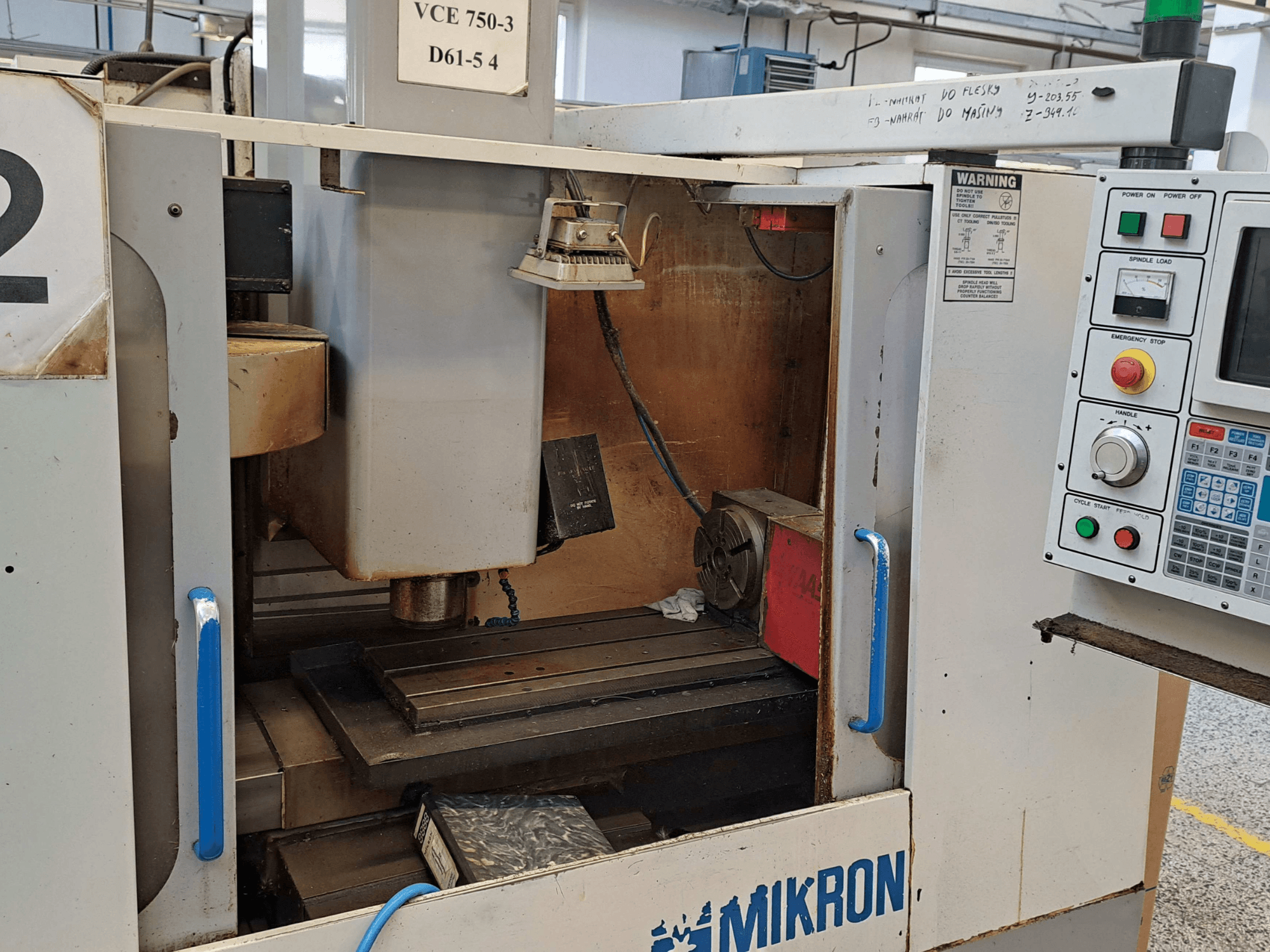 Vooraanzicht van een Mikron VCE 750-3 freesmachine, met de spindel, het bedieningspaneel en de werktafel met technische details.