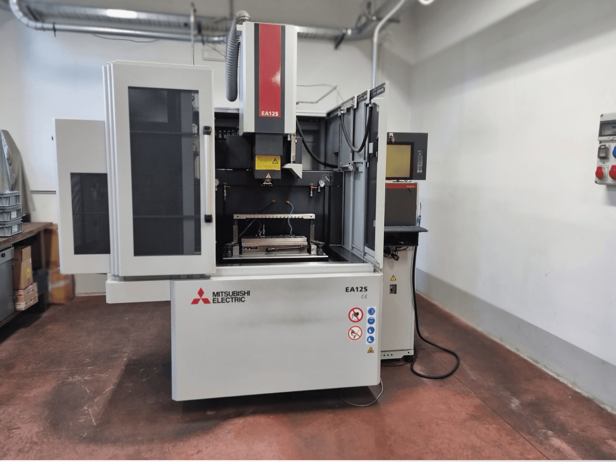 Mitsubishi Electric EA12S draadsnijmachine, vooraanzicht, met open deuren, bedieningspaneel en veiligheidslabels.