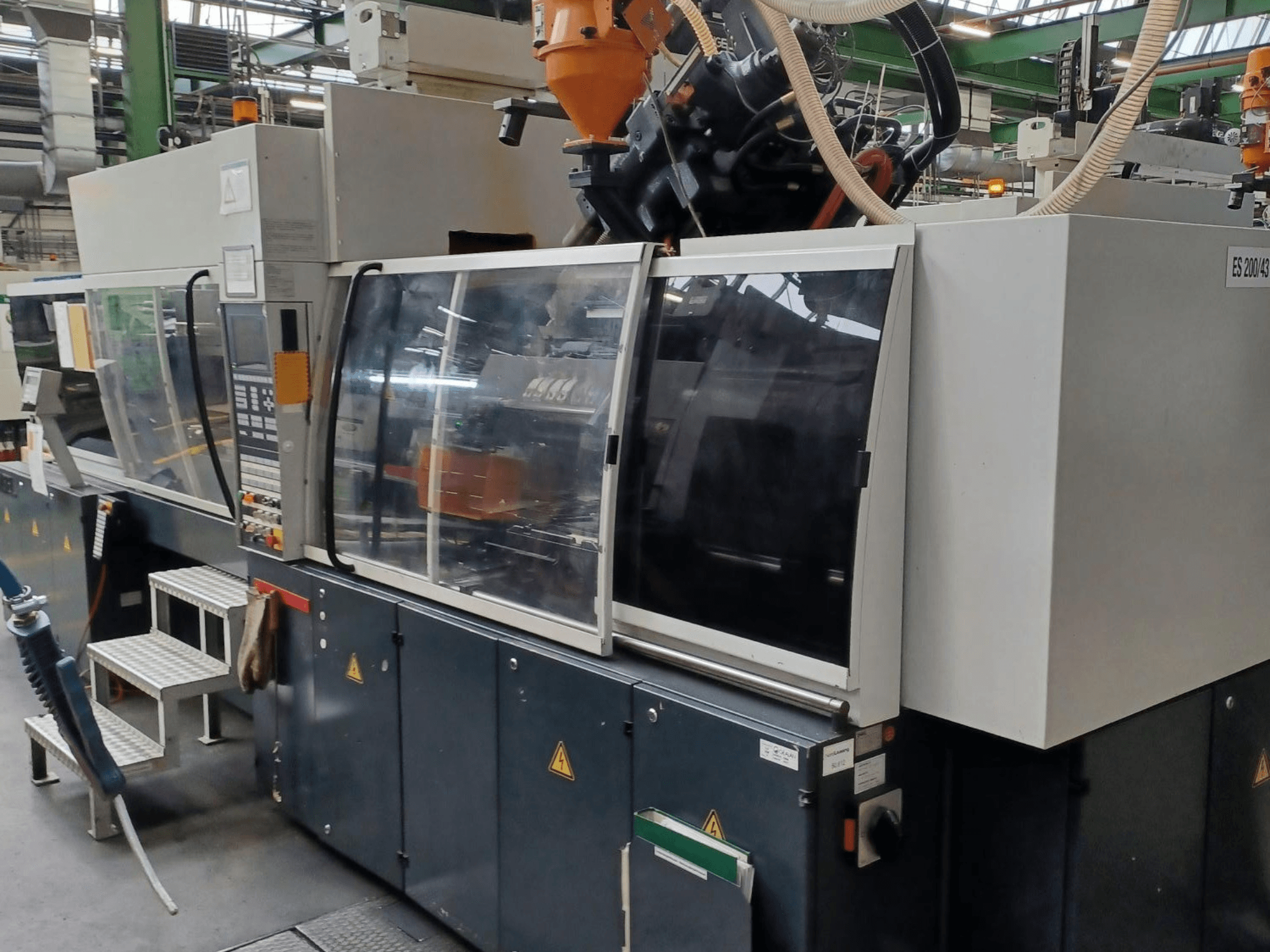 Vooraanzicht van een kunststof spuitgietmachine, merk en model onbekend, met transparante veiligheidsdeuren en bedieningspaneel.