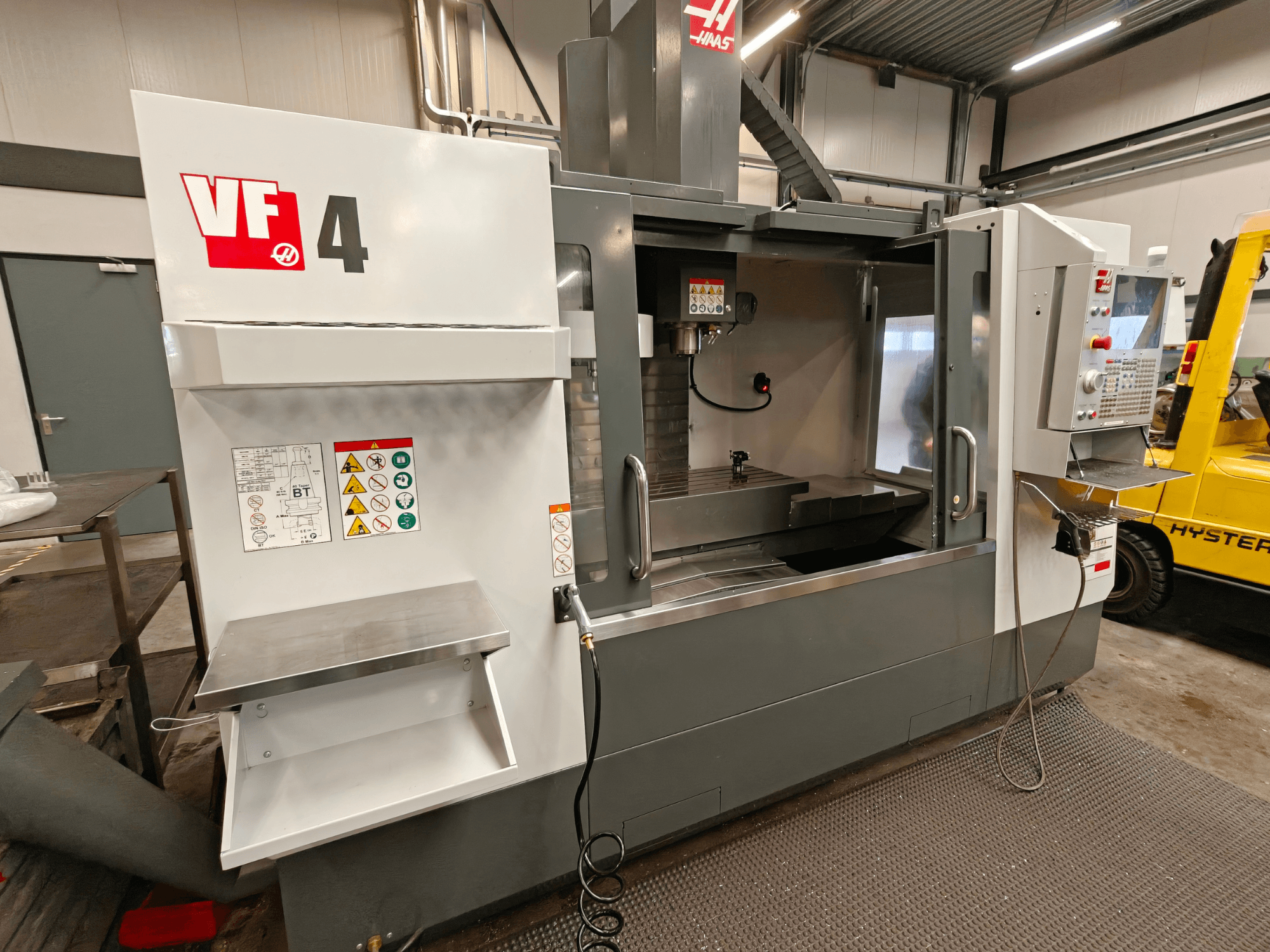 HAAS VF-4 verticaal bewerkingscentrum, vooraanzicht, met bedieningspaneel, werkgebied en veiligheidslabels aan de zijkant.